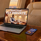 A laptop and a phone in a private jet cabin, showing Work hard, fly private and Dream it, own it from AMBITION Vol. 3